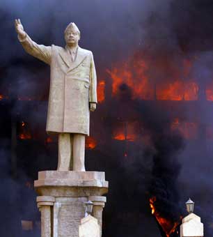 A statue of Saddam Hussein stands in front of the burning National Olympic Committee building in Baghdad, on April 19, 2003. (Photo: Tyler Hicks / The New York Times)